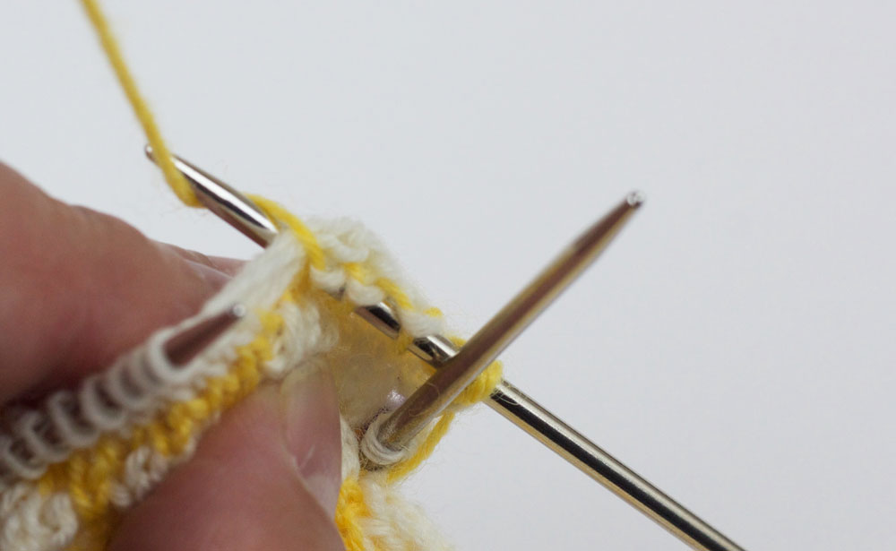 Eine nachträglich eingestrickte Ferse für die CajaSocks - Der Faden wird um die Nadel gelegt und es wird eine Masche rechts gestrickt. Dabei werden die Querfäden umfasst.