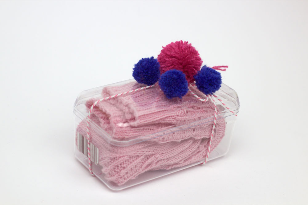 Socken verpacken - Pompons in unterschiedlichen Größen werden auf einer mit Socken gefüllten Dose befestigt.