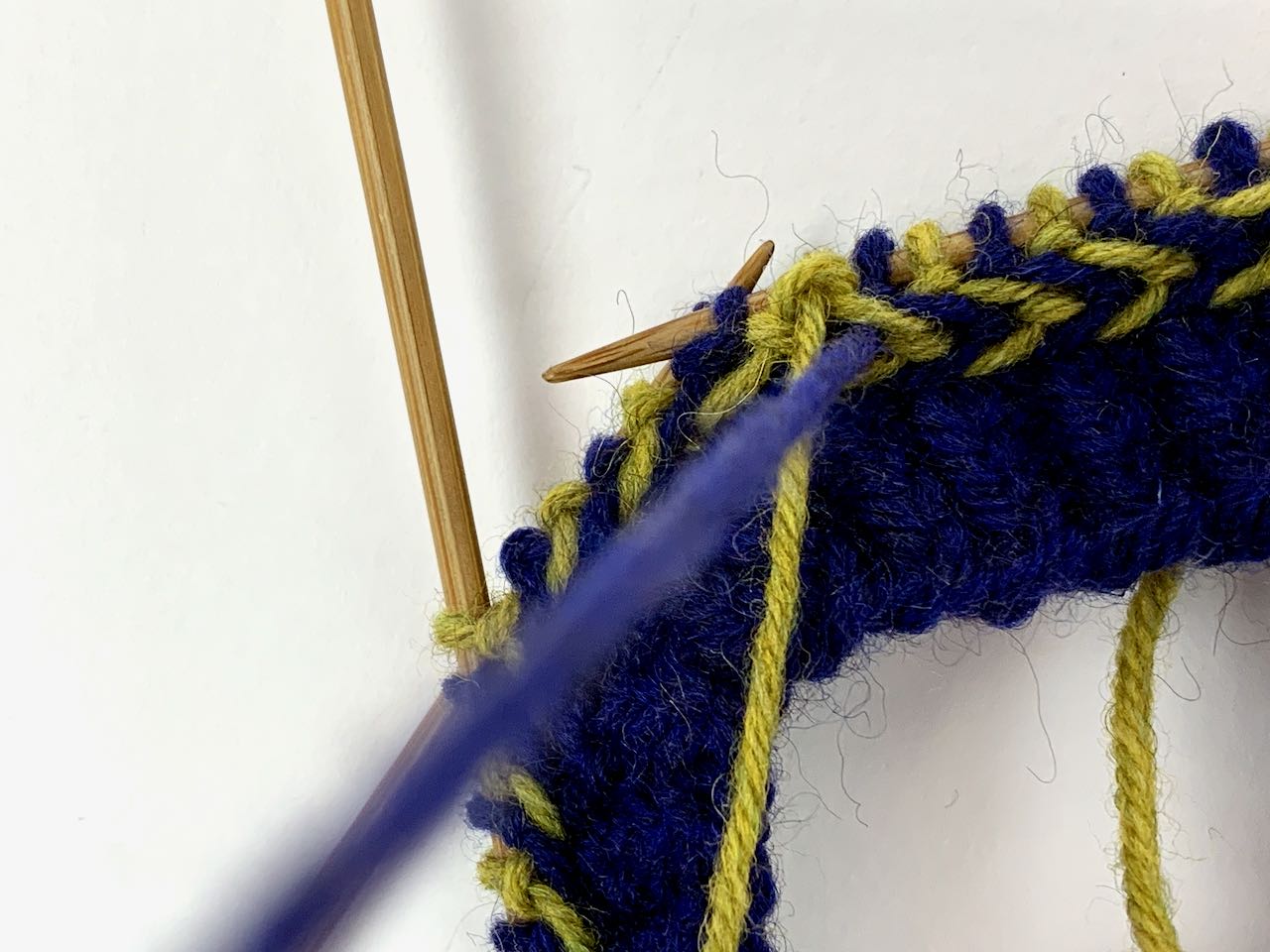 Bei Teil 2 der lettischen Borte wird der Faden für die zu strickende blaue Masche über den gelben Faden geführt.