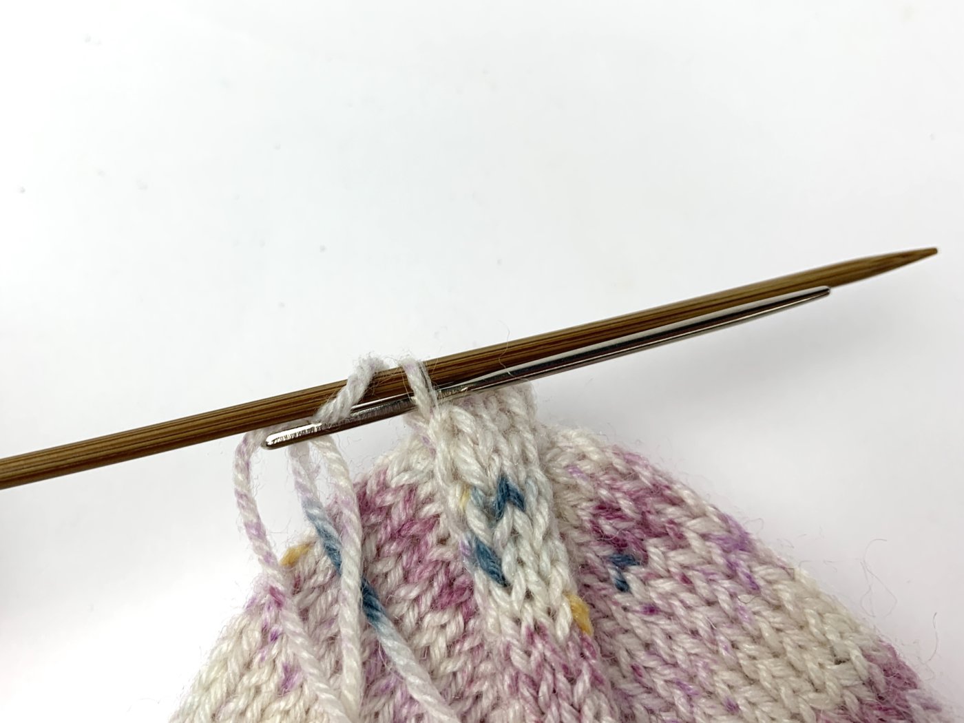 Schiebe die Nähnadel wie zum Rechtsstricken durch die letzte Masche auf der vorderen Nadel und lasse sie von der Stricknadel gleiten.