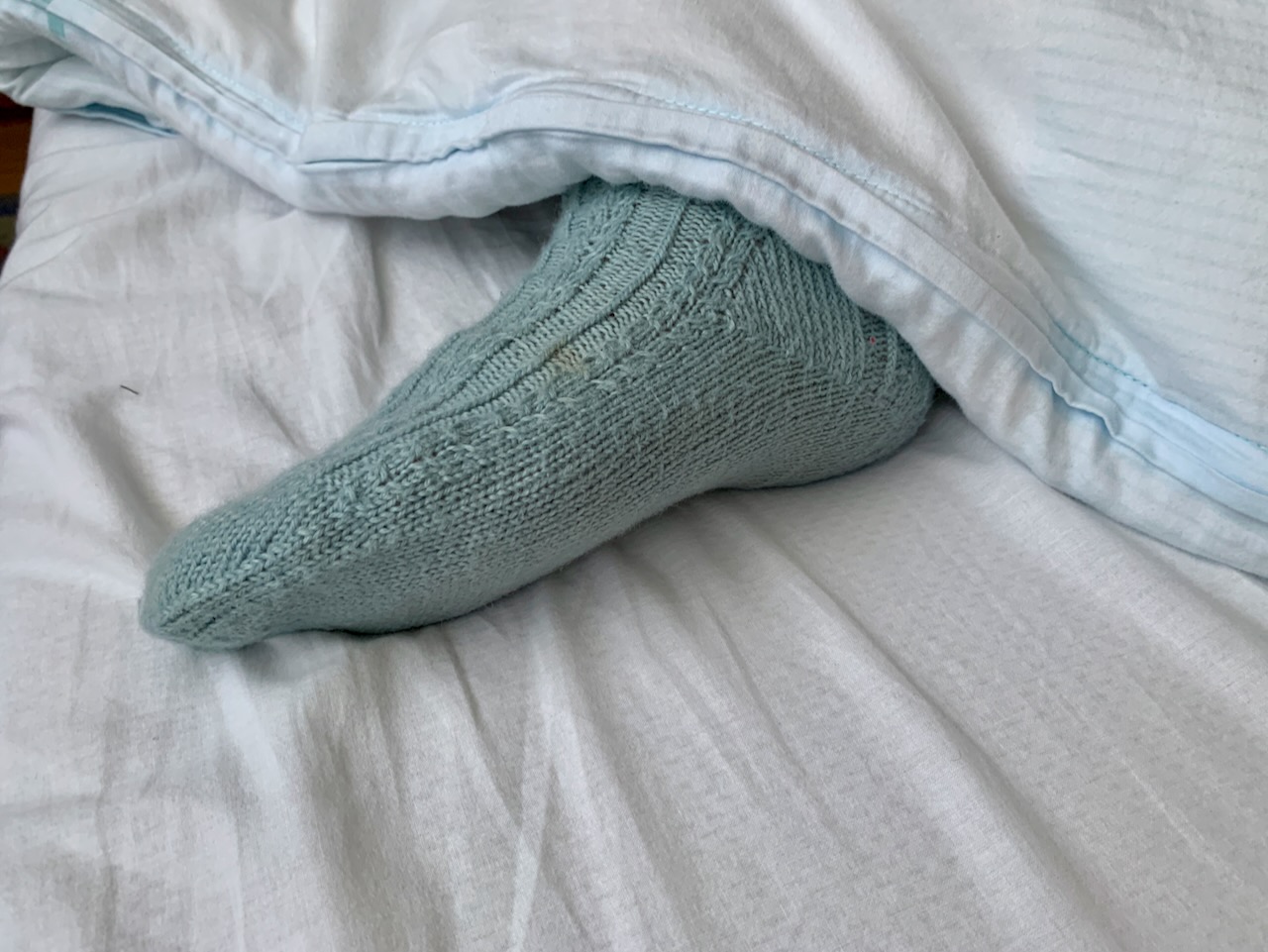 Bettsocken - Fuß guckt unter dem Oberbett heraus