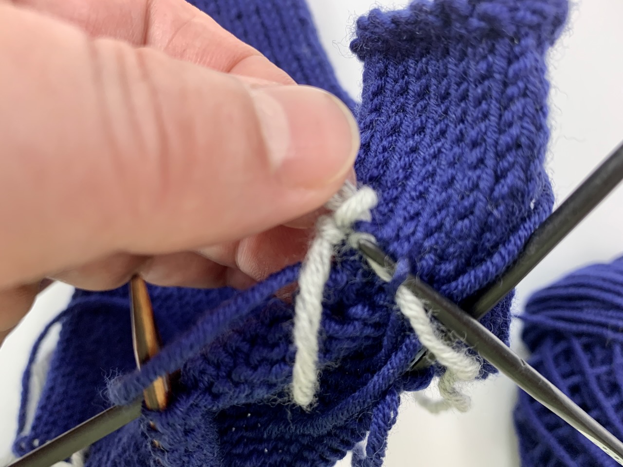 Dei Stegmaschen für den kleinen Finger wurden mit dem prov. Maschenanschlag gebildet. Nach dem nun der Ringfinger an die Reihe kommt, wird der prov. Maschenanschlag aufgelöst und die Maschen auf eine Stricknadel gezogen.